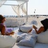 Due persone rilassate su divani bianchi in spiaggia con drink in mano.