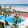 Vista su piscina, campo da tennis e spiaggia con mare azzurro sullo sfondo.