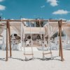 Beach club con sedie bianche, altalene e tende su sabbia.