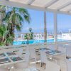 Terrazza con tavoli bianchi vista piscina, palme e mare sullo sfondo.