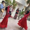 Due bambine in abiti rossi danzano mentre un gruppo suona strumenti musicali all'aperto.