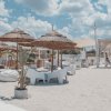 Spiaggia con sedie, ombrelloni in paglia e cielo nuvoloso.