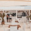 Un bar all'aperto con mobili in legno bianco, sedie e piante tropicali.