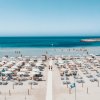 Spiaggia affollata con ombrelloni bianchi e mare calmo.