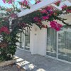 Edificio bianco con pergolato coperto di fiori rosa e ingresso con grandi porte finestra.