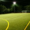 Campo da calcio illuminato di notte con alberi sullo sfondo.
