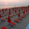 Spiaggia al tramonto con lettini e ombrelloni chiusi.